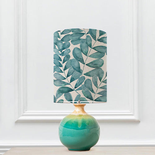 A ceramic lamp with a blue lamp shade featuring a printed design of botanical leaves.