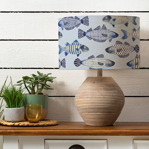 A coastal lamp shade with a printed design of various fish in a range of light and deep blue shades.