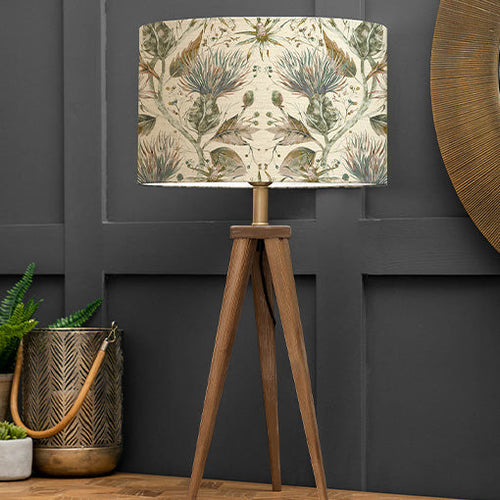 A country table lamp with a botanical wildflower design, placed on a wooden table in front of a dark grey wall.