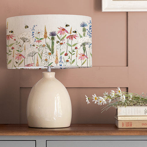 A floral table lamp with a colourful garden flower design and a cream ceramic lamp base.