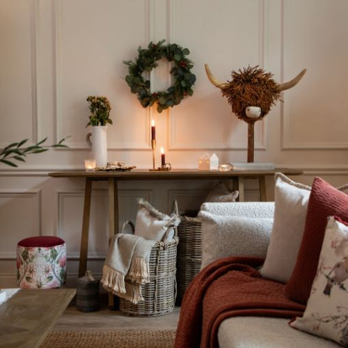 A collection of winter themed homeware, including red coloured throws, cushions, a wooden cow sculpture, festive wreaths and a footstall.