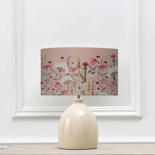 A pink lamp shade with a garden floral design, placed on a white ceramic lamp base.